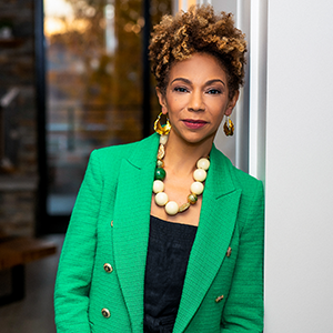 a woman in a green jacket leaning on a wall