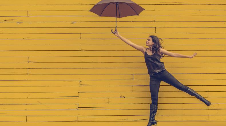 woman leaping with an umbrella in front of a yellow wall