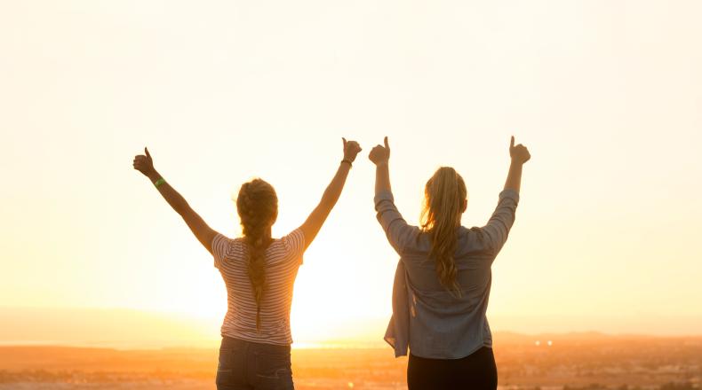 two women giving thumbs up to rising sun