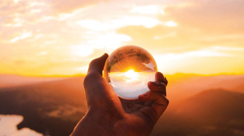hand holding a crystal ball with a sunset and mountains in the background