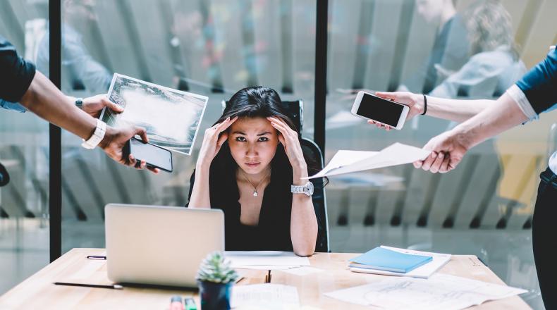 woman holding her head with people handing her papers