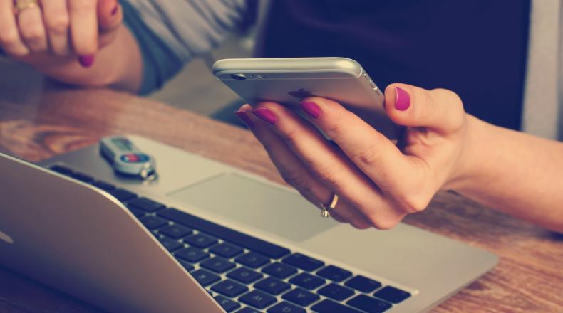 woman holding an iphone in front of open laptop