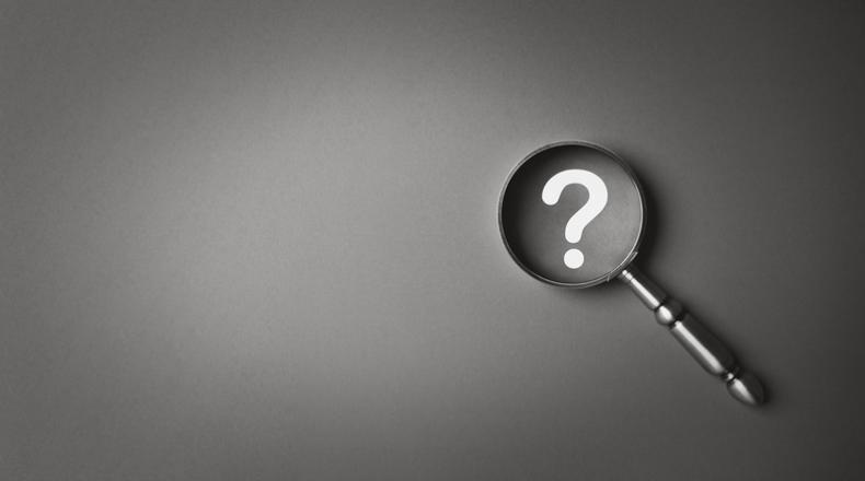 Black and white magnifying glass and question mark icon symbol on gray paper background with copy space.