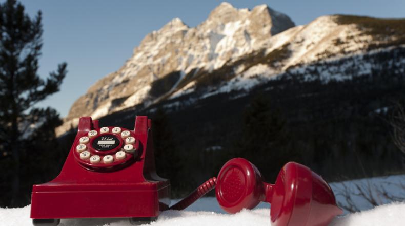 red dial telephone sitting on snow with mountain in background