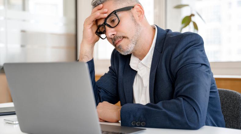 Mature gray-haired 60s businessman staring at computer scratching head stock photo