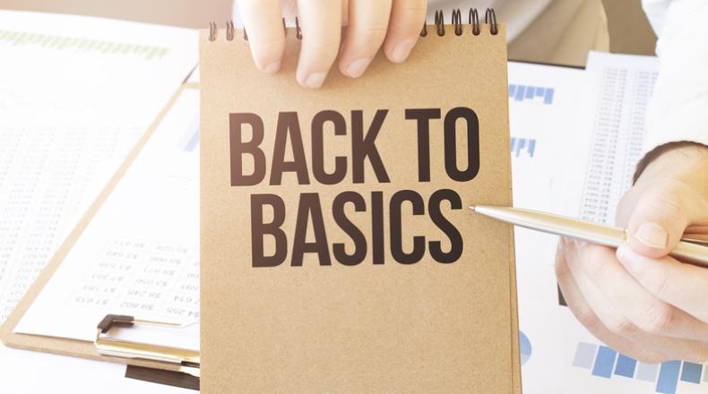 Text BACK TO BASICS on brown paper notepad in businessman hands on the table with diagram.