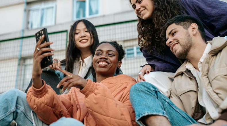 group of young multi-ethnic individuals looking at something on a cell phone; Gen Z concept