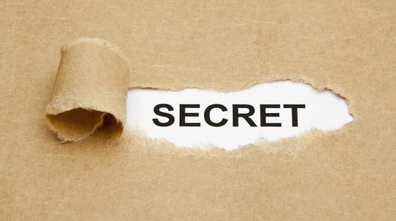 Secret Concept stock photo; torn brown paper reveals word secret in black lettering on white background