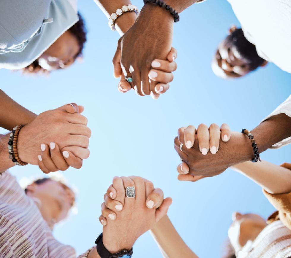 Diversity, support and people holding hands in trust and unity for community against sky background