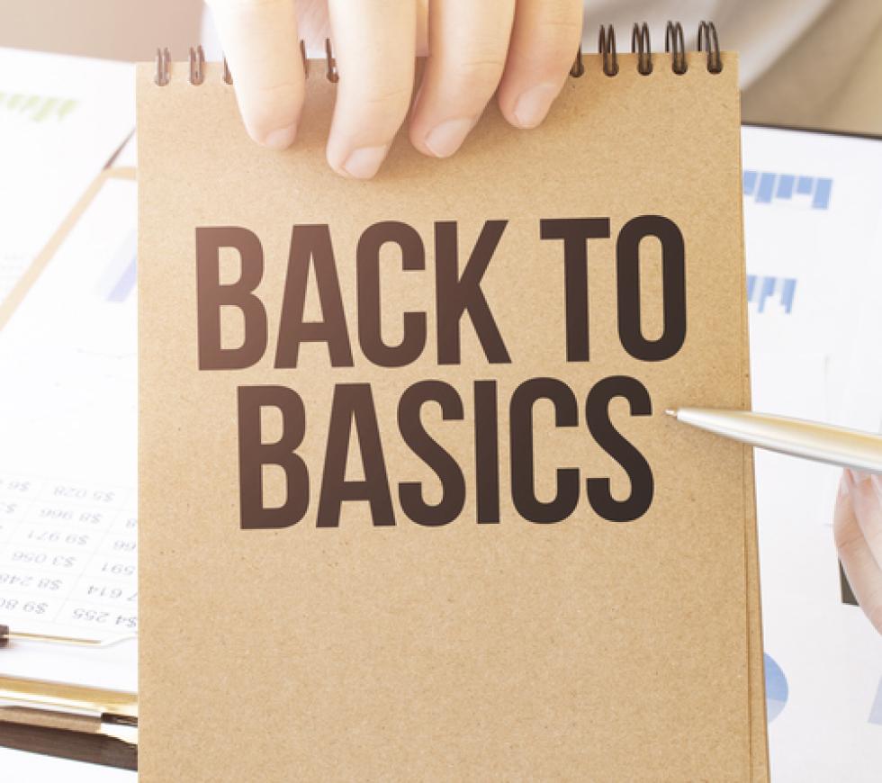 Text BACK TO BASICS on brown paper notepad in businessman hands on the table with diagram.