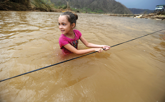 Ruby Rodriguez, 8, looks back at her mother as she wades across the San Lorenzo de Morovis River with her family. The bridge was swept away by Hurricane Maria on Wednesday, Sept. 27, 2017. They were returning home after visiting family on the other side (AP photo, Gerald Herbert).