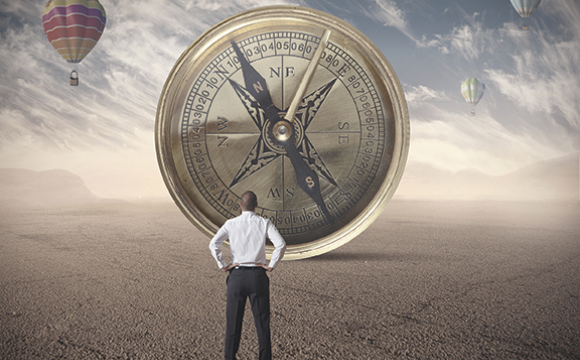 Man looking at a large compass with a hot air balloon in the background