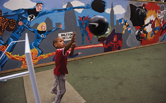 Young boy playing ball with superheroes painted on the wall behind him