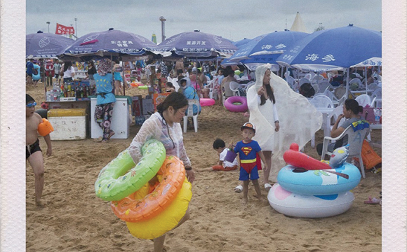 Woman and child on a beach carrying inflatable rafts
