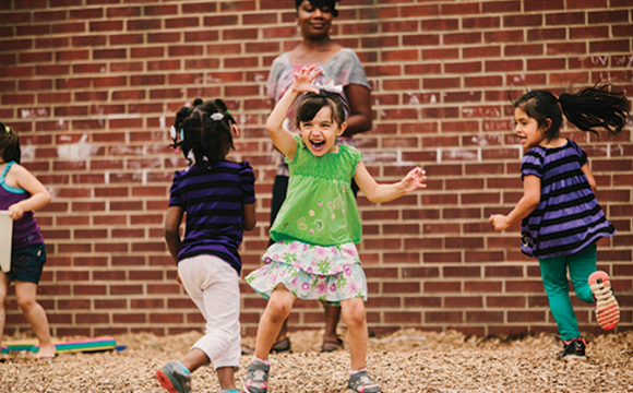 Children playing while a woman looks at them smiling