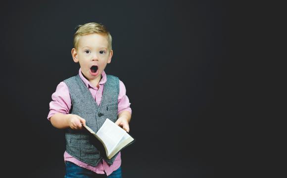 boy in pink shirt and grey vest reading a book and surprised 