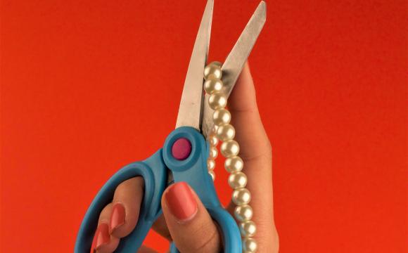 a hand holding scissors to a pearl necklace