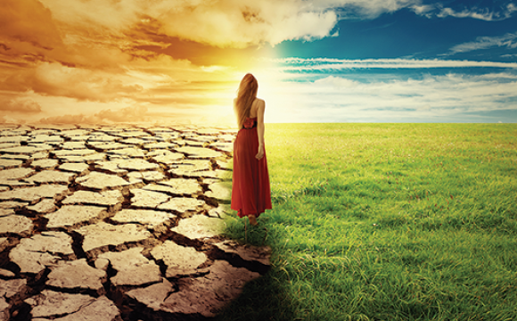 woman standing in the middle of a cracked ground and a green grass with a stormy sky