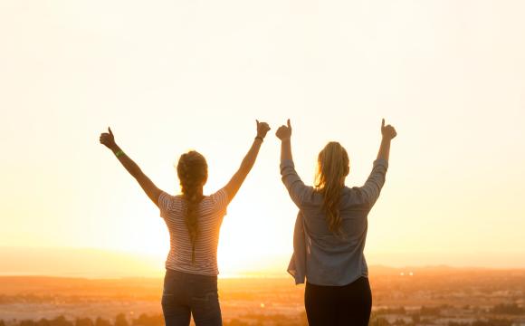two women giving thumbs up to rising sun