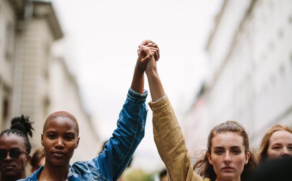 a black woman and a white woman holding hands in the air to show unity