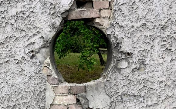 grey concrete brick wall with hole looking over green grass and tree