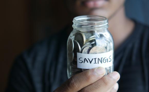 a man holding a glass jar of coins with word savings on it