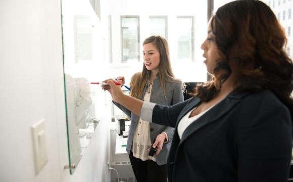 Two people writing on a glass wall 