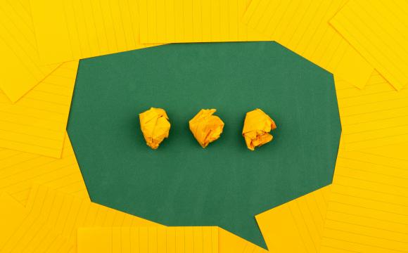 yellow sheets of paper lie on a green school board and form a chat bubble with three crumpled papers.