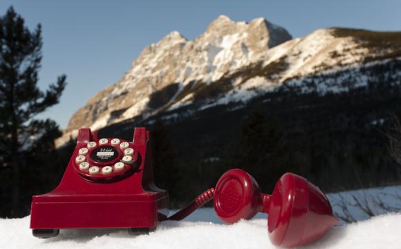 red dial telephone sitting on snow with mountain in background