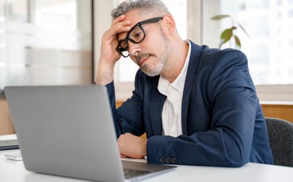 Mature gray-haired 60s businessman staring at computer scratching head stock photo