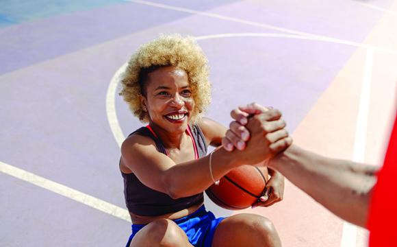 person grasping the hand of a woman with a basketball sitting on a basketball court