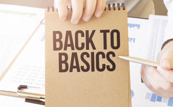Text BACK TO BASICS on brown paper notepad in businessman hands on the table with diagram.