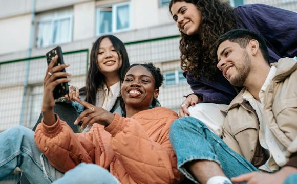 group of young multi-ethnic individuals looking at something on a cell phone; Gen Z concept